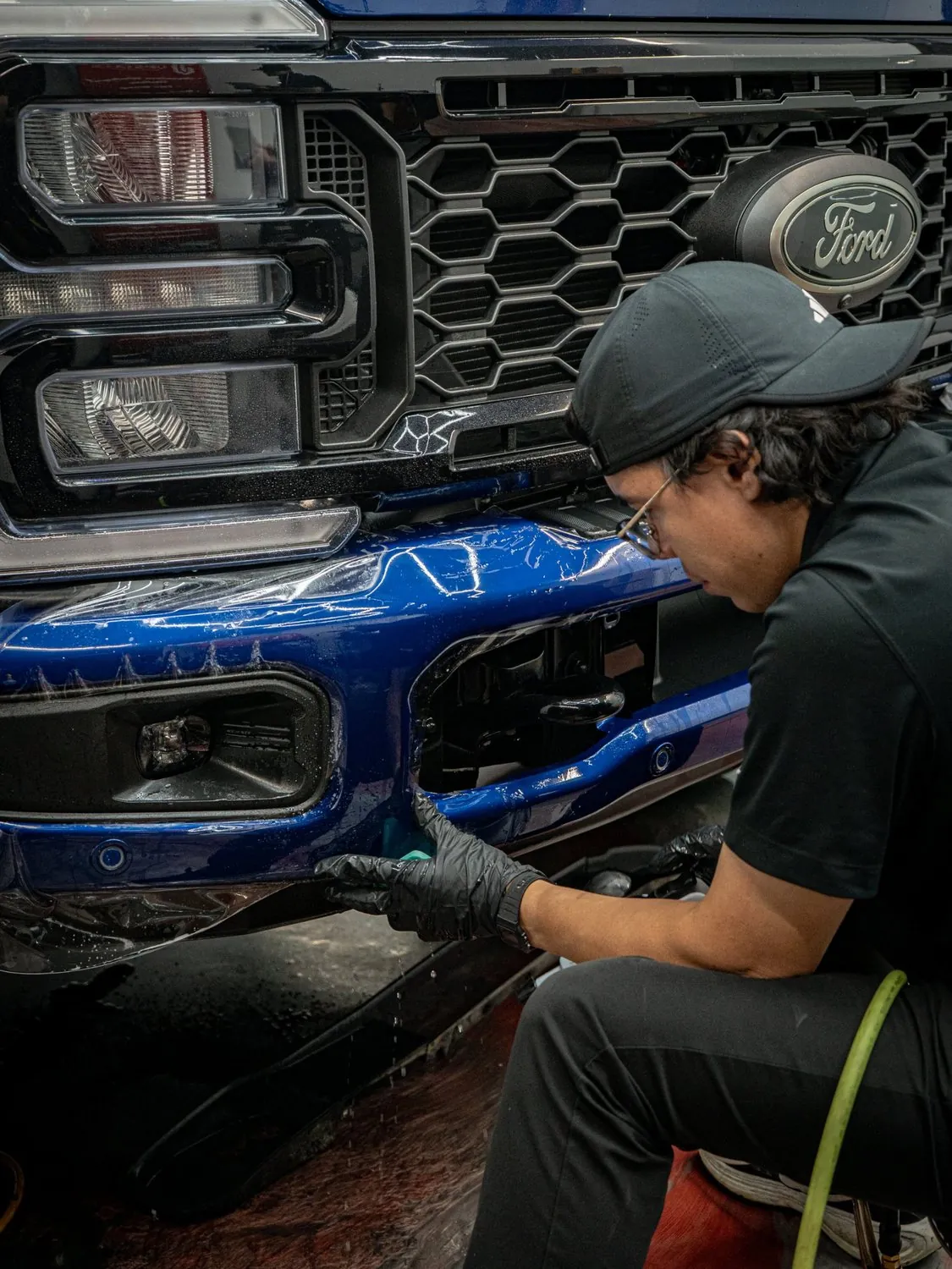 Installer squeegeeing paint protection film on a Ford bumper